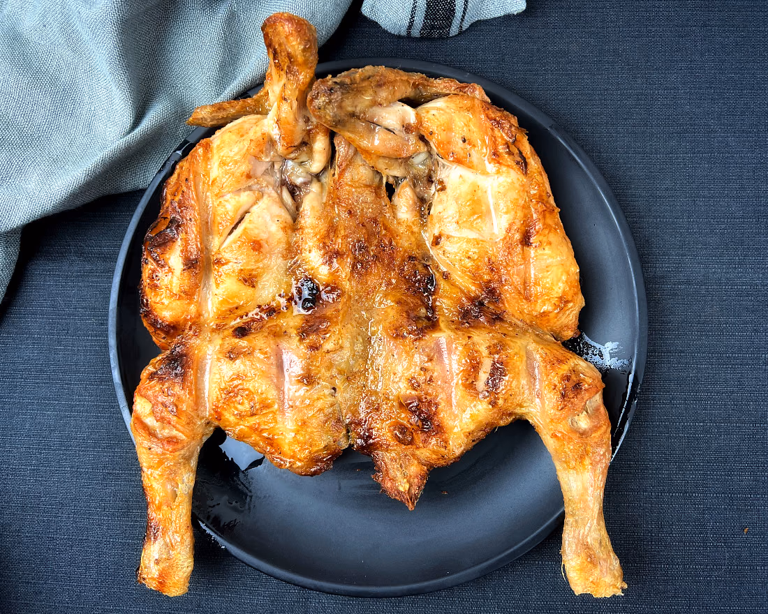 Frango inteiro assado no carvão, aberto e dourado, num prato preto